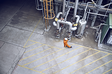 Worker in an orange jumpsuit walking near industrial pipes and equipment