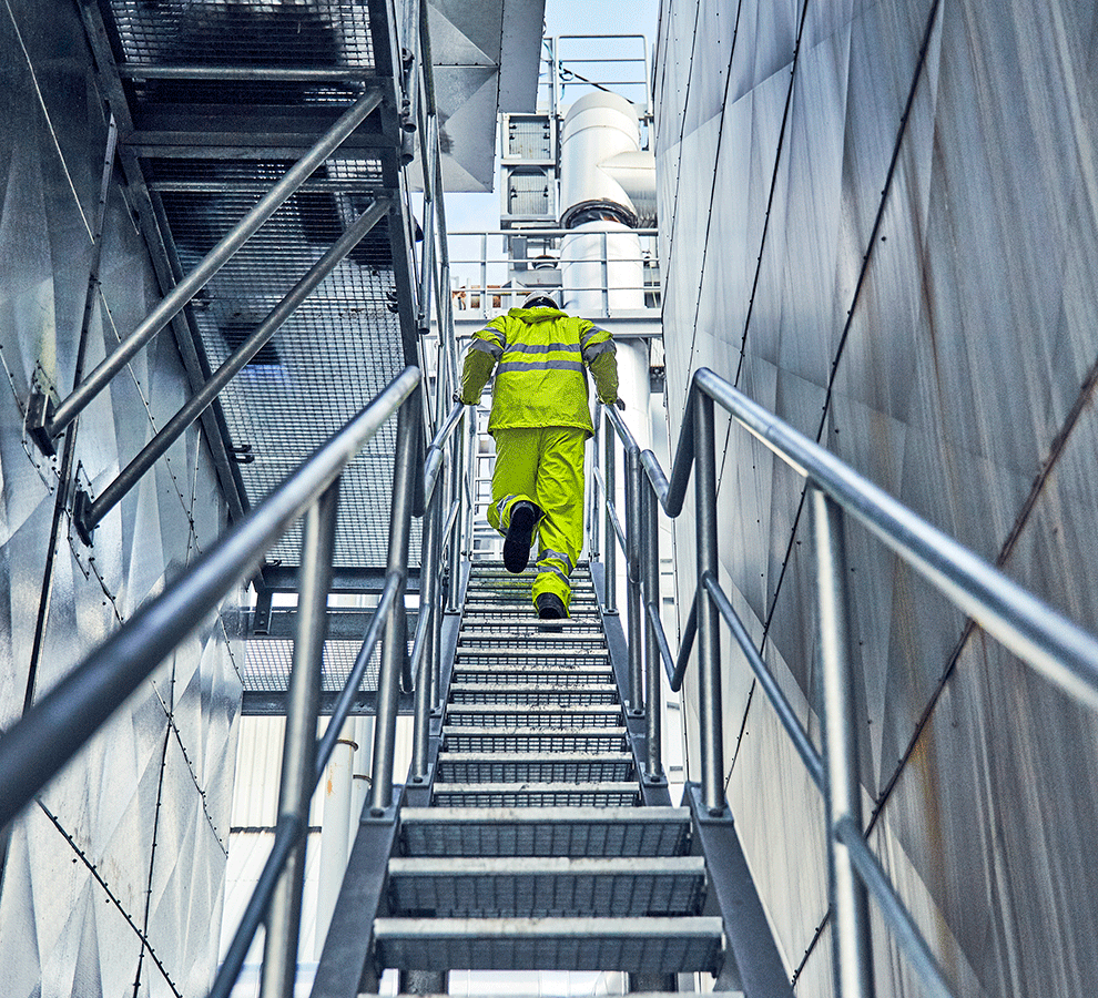 Worker in climbing an industrial staircase next to large processing equipment